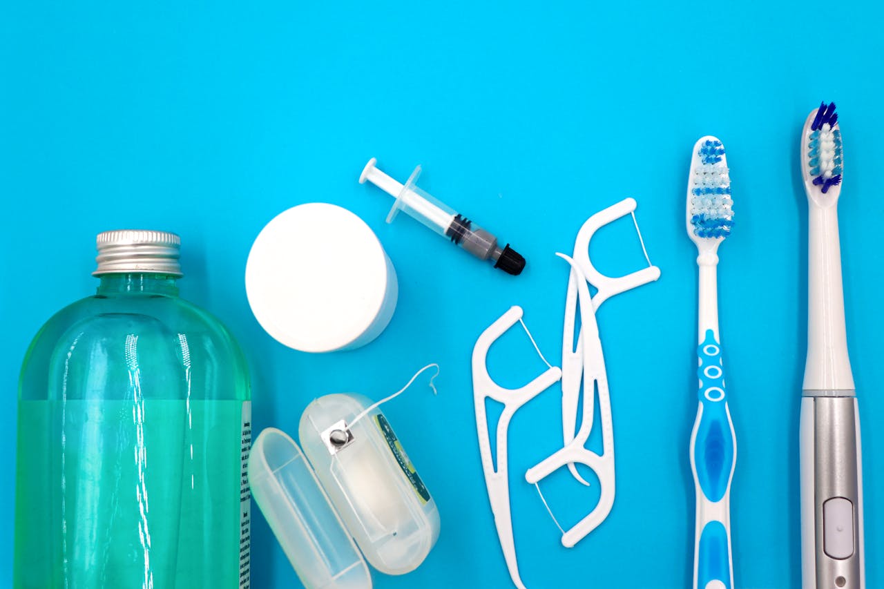 Flat lay of oral hygiene essentials including toothbrushes, floss, and mouthwash on a blue surface.