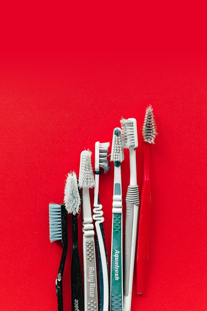 Collection of old and worn toothbrushes on a bright red background, highlighting dental hygiene concepts.