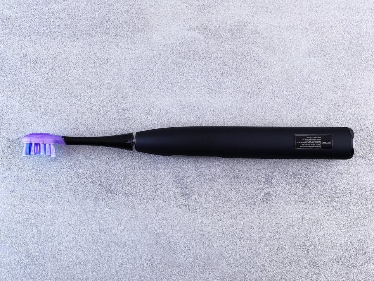 A sleek black electric toothbrush with a purple head lies on a textured concrete surface.